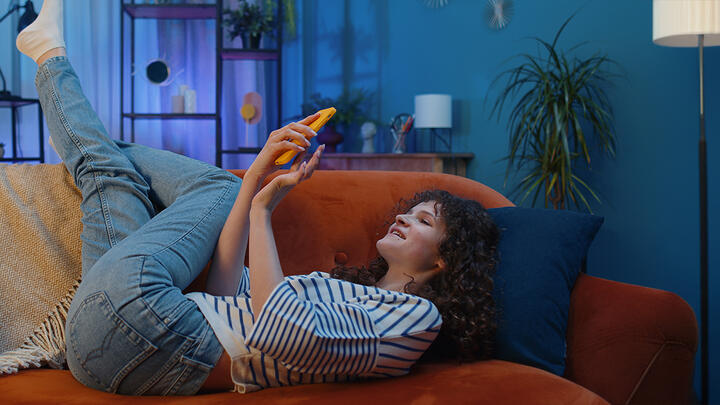 Woman on her back on a comfy couch and fun room, shoppping online on her phone